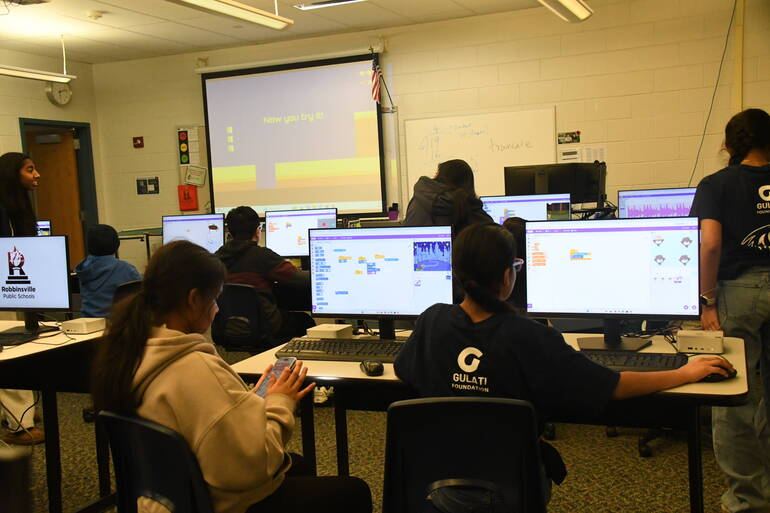 A Scratch coding workshop, with a volunteer in a Gulati Foundation shirt